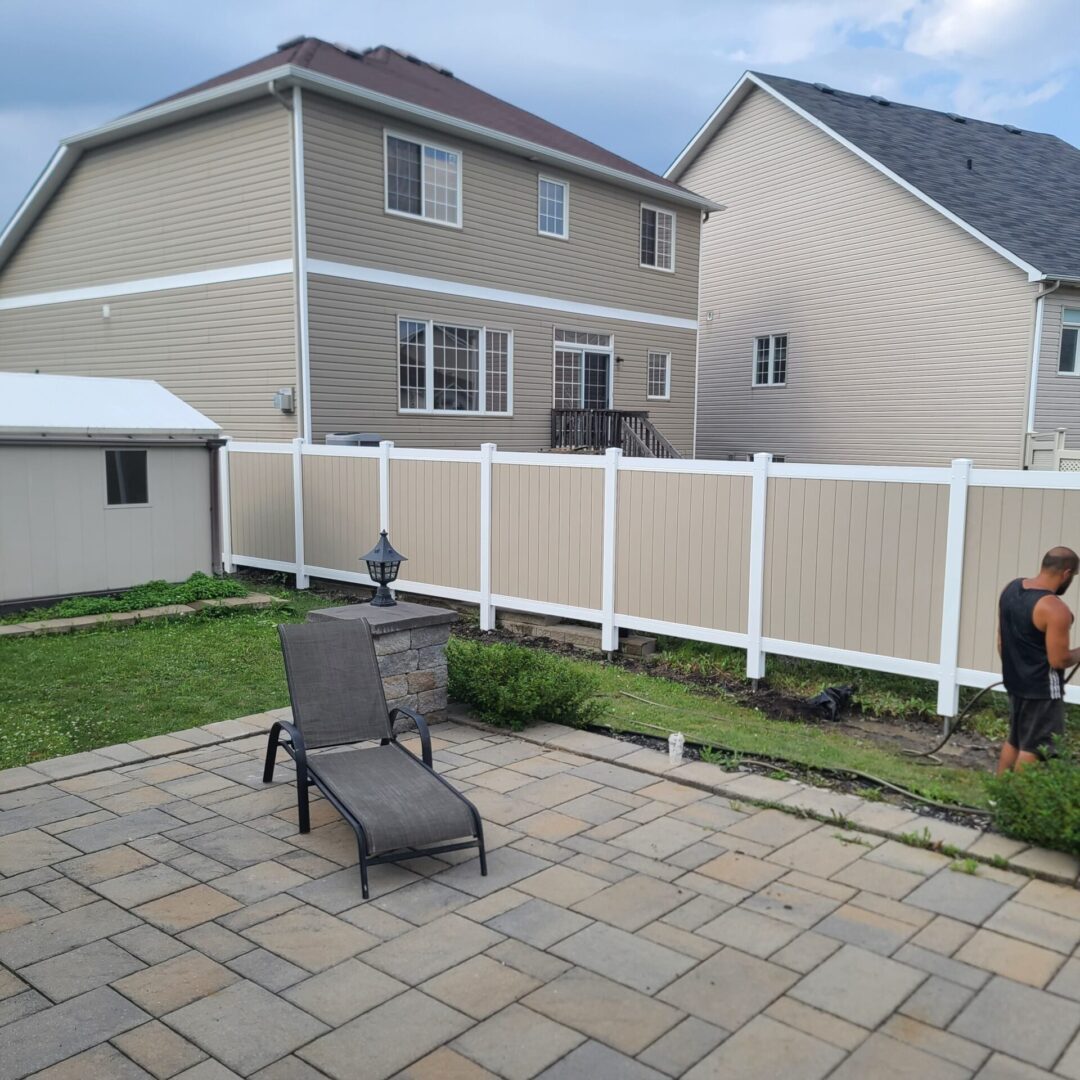 Tan and White Fence Backyard with patio, chairs, and houses.