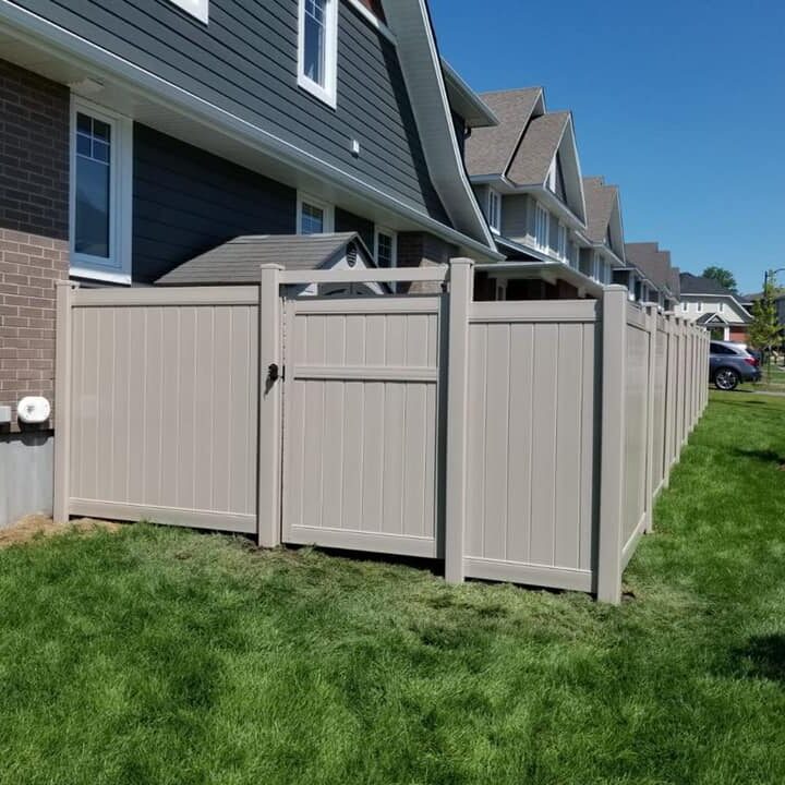 Tan Gate and front of yard House with beige fence and green lawn.